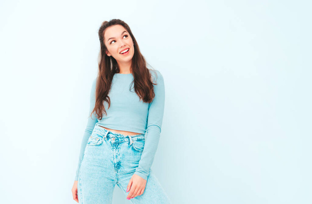 Young beautiful smiling female in trendy summer hipster clothes. Sexy carefree woman posing near light blue wall in studio. Positive model having fun indoors. Cheerful and happy  - 写真・画像