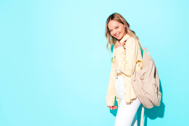 Young beautiful woman looking at camera.Trendy female smiling in casual summer clothes. Positive and funny model posing on grey background in studio with backpack - Zdjęcie, obraz