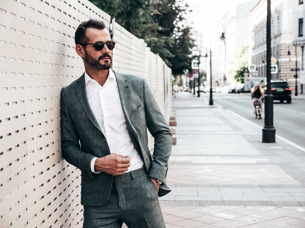 Portrait of handsome confident stylish hipster lambersexual model.Modern man dressed in elegant suit. Fashion male posing in the street background in Europe city at sunset. In sunglasses - Zdjęcie, obraz