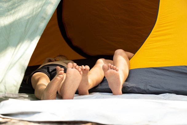 pies de los niños que sobresalen de una tienda de campaña acampando en el bosque bajo el sol, pies de los niños en un palo, acampando - Foto, imagen