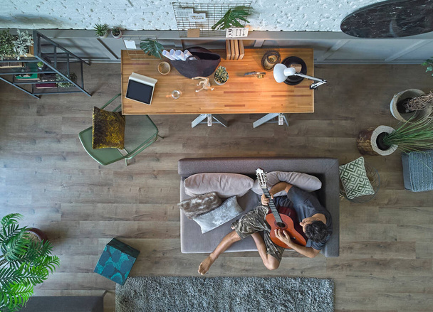 Człowiek mieszka w domu koncepcja z sofą i stylu stołowym, gra na gitarze, w górę koncepcji domu fotografowania. - Zdjęcie, obraz