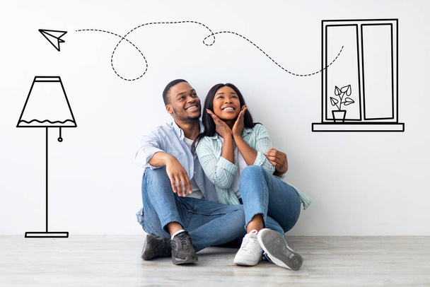 Αγαπώντας αφροαμερικανό ζευγάρι φαντάζεται εσωτερικό του διαμερίσματός τους, κάθεται στο πάτωμα κοντά στον τοίχο με σχέδια doodle - Φωτογραφία, εικόνα