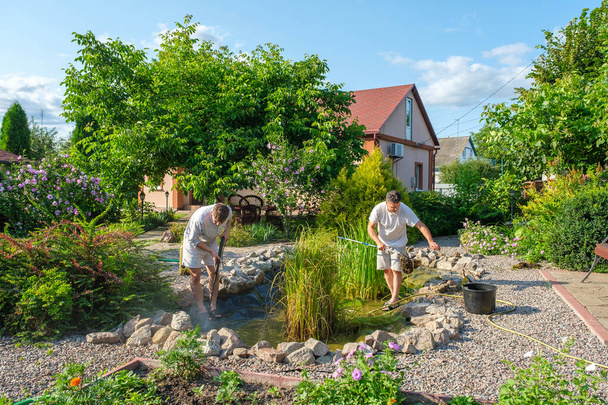 Πατέρας και γιος καθαρισμού του πυθμένα της λίμνης κήπο με υψηλής πίεσης πλυντήριο από λάσπη  - Φωτογραφία, εικόνα