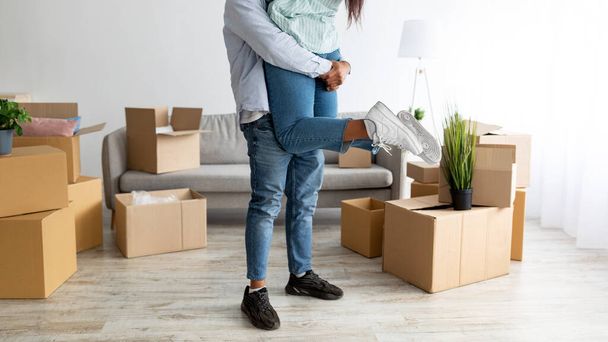 Mudando-se para a própria casa. Amante marido negro levantando sua esposa e se divertindo entre caixas em novo apartamento, colheita - Foto, Imagem