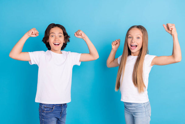 Φωτογραφία από δύο παιδιά χαρά αυξήσει γροθιές ανοιχτό στόμα πρωταθλητής διάθεση φορούν λευκό t-shirt απομονωμένο μπλε χρώμα φόντο - Φωτογραφία, εικόνα