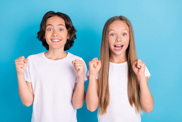 Photo of two astonished children celebrate victory raise fists wear white t-shirt isolated blue color background - Foto, Imagem