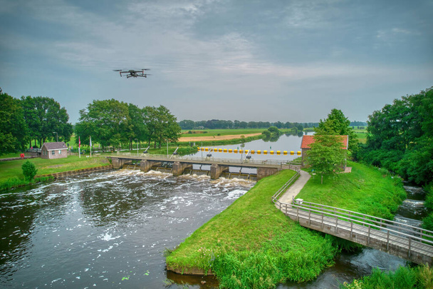 Een luchtfoto met drone op de achtergrond boven een stuw in de Vecht in Nederland. Stroomafwaarts, Sluiswachtershuis naast de brug. Vispas, visladder. Overijssel Vecht. - Foto, afbeelding