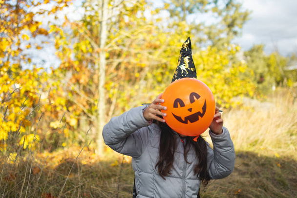 Halloween kids. Little girl with jack o' lantern in witch hat with pumpkin. Toddler kid in witch costume playing in autumn park. A Child in a carnival costume outdoors - 写真・画像