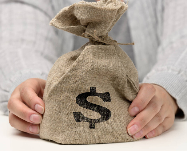 mano sostiene una bolsa de lona llena de dinero con un icono del dólar estadounidense sobre un fondo blanco. Concepto de planificación presupuestaria, beneficios y ahorros, resultado financiero final - Foto, imagen
