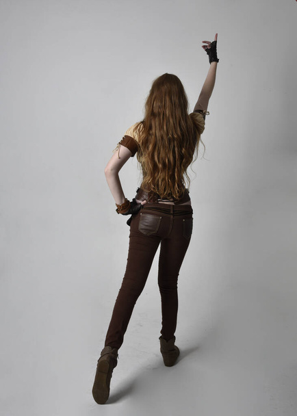 Uzun kızıl saçlı, Steampunk 'tan esinlenilmiş bir kostüm giymiş güzel bir genç kadının tam boy portresi. Stüdyo arka planında hareketli poz. - Fotoğraf, Görsel