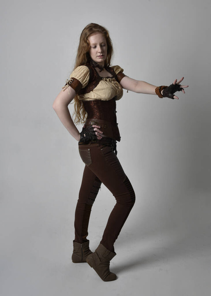 Retrato de comprimento total de bela jovem com cabelo vermelho longo, vestindo traje inspirado steampunk. Ação em pé pose isolada no fundo do estúdio. - Foto, Imagem
