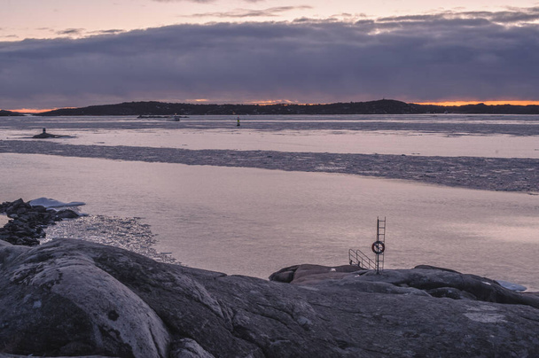 απότομους βράχους δίπλα σε ένα παγωμένο φιόρδ το χειμώνα. Πλοία στο βάθος, μετά το ηλιοβασίλεμα. - Φωτογραφία, εικόνα