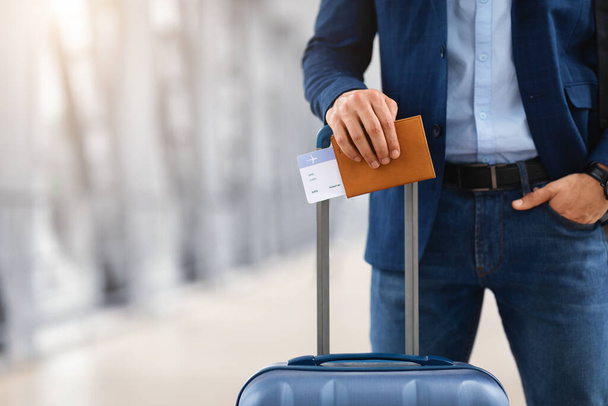 Έτοιμος για ταξίδι. Αγνώριστος άνθρωπος στέκεται με βαλίτσα, διαβατήριο και αεροπορικά εισιτήρια - Φωτογραφία, εικόνα