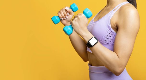 Unrecognizable african american lady exercising with two blue dumbbells, wearing fitness tracker with blank screen - Foto, Imagen