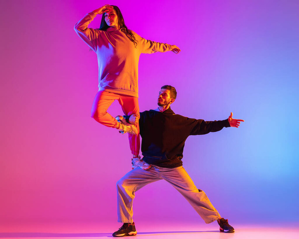 Gündelik kıyafetlerle dans eden iki genç adam ve kız pembe arka planda neon ışıkta hip-hop yapıyorlar.. - Fotoğraf, Görsel