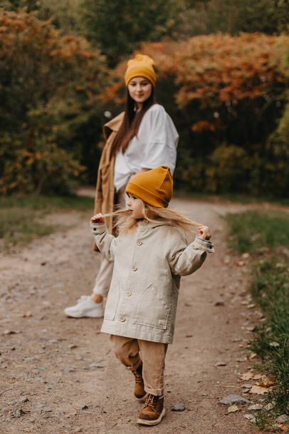 Young happy and smiling mom with her little daughter in arms hugging and kissing spending a weekend on a walk in autumn park. selective focus, noise effect, Autumnal mood - Фото, зображення