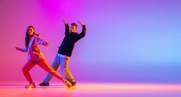 Flyer. Two young people, guy and girl dancing contemporary dance, hip-hop over pink background in neon light. - Photo, Image