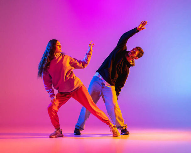 Дві молоді, хлопець і дівчина в повсякденному одязі танцюють сучасний танець, хіп-хоп на рожевому фоні в неоновому світлі
. - Фото, зображення
