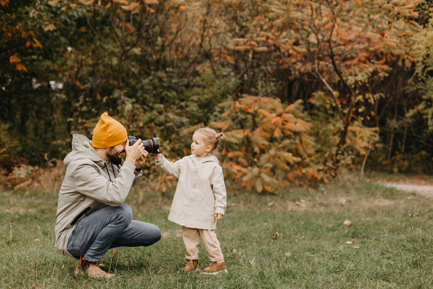 happy father and daughter playing while walking in a beautiful autumn park. Ideal weekend father with his little daughter. Dad takes a picture of his daughter on a professional camera - Foto, Bild