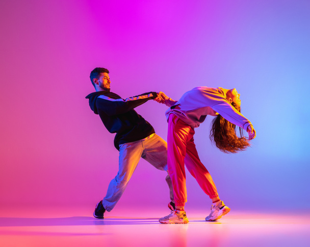 Two young people, guy and girl in casual clothes dancing contemporary dance, hip-hop over pink background in neon light. - 写真・画像