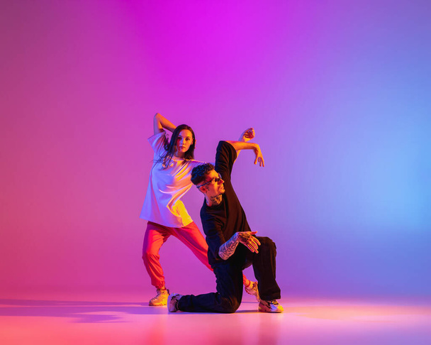 Дві молоді, хлопець і дівчина в повсякденному одязі танцюють сучасний танець, хіп-хоп на рожевому фоні в неоновому світлі
. - Фото, зображення