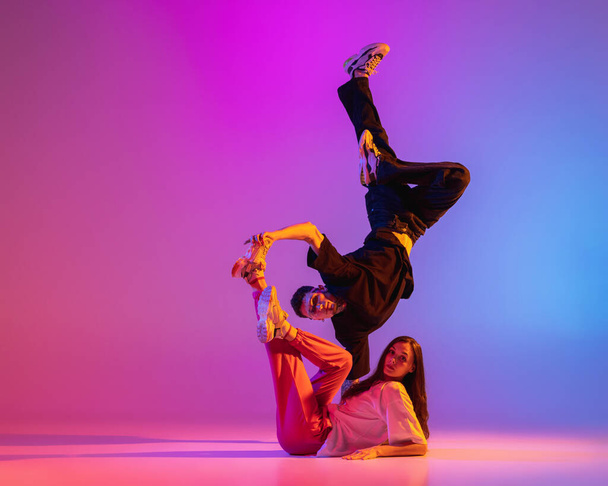 Gündelik kıyafetlerle dans eden iki genç adam ve kız pembe arka planda neon ışıkta hip-hop yapıyorlar.. - Fotoğraf, Görsel