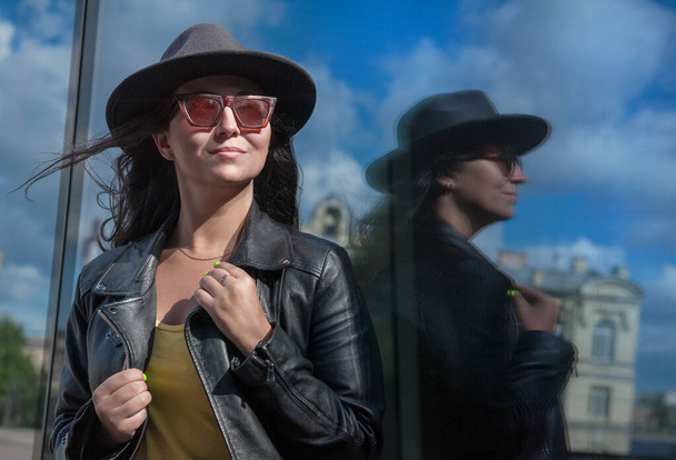 Gyönyörű fiatal nő sapkával és napszemüveggel a városháza tükörfalának közelében - Fotó, kép