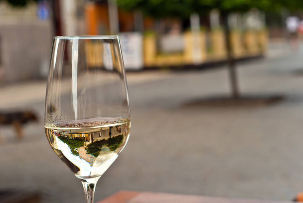 Glass of white wine close up. Alcoholic drink on a wooden table on a background of the city. Transparent wine on the summer terrace of the restaurant. - Fotografie, Obrázek