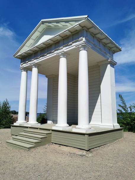 Świątynia Neptuna z białymi kolumnami w skalistym parku naturalnym Monrepos miasta Vyborg na tle błękitnego nieba z chmurami. - Zdjęcie, obraz