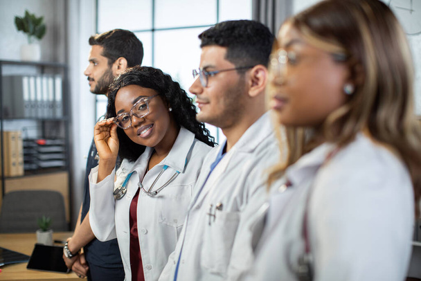 Profile portrait. Multiracial group of four doctors in lab coats standing in a row. - Foto, afbeelding