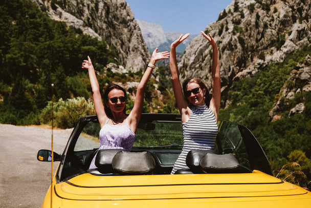 Two young woman in yellow car enjoying vacation - Fotó, kép