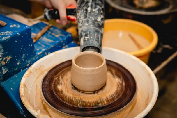 Potter working on potters wheel with clay. Process of making ceramic tableware in pottery workshop. Handicraft and art concept. - Фото, изображение