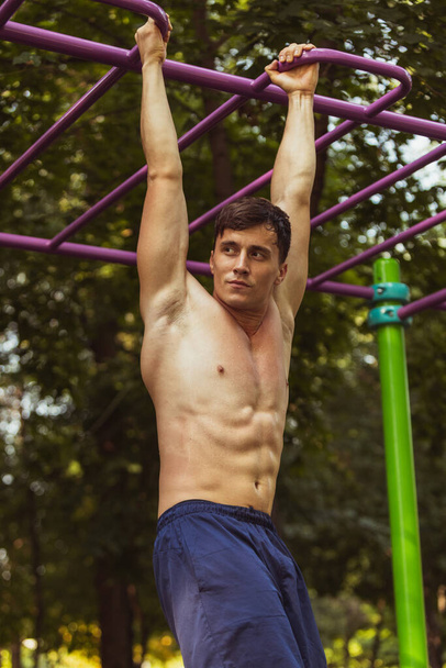 One young handsome caucasian man in sportswear training, exercising on sports ground outdoors on bright summer day. - Foto, afbeelding