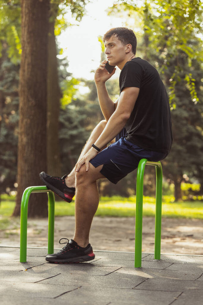 Spor giyimli genç beyaz adam yaz günü spor sahasında telefonla konuşuyor.. - Fotoğraf, Görsel