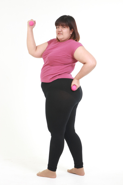 アジア系の太った女性は、ピンクのダンベルを持ったワークアウト服を着て、白い背景に立っています。健康管理の概念と健康のための減量 - 写真・画像