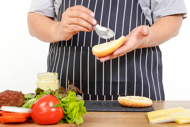 λίπος άνθρωπος μαγείρεμα Κρατήστε ψωμί και βούτυρο για να κάνει χάμπουργκερ. Η έννοια του μαγειρέματος για να χάσουν βάρος, τρώνε υγιεινά τρόφιμα. λευκό φόντο - Φωτογραφία, εικόνα