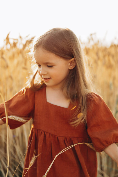 pretty 3-year-old girl walks and poses for a photo in a wheat field at sunset - Valokuva, kuva