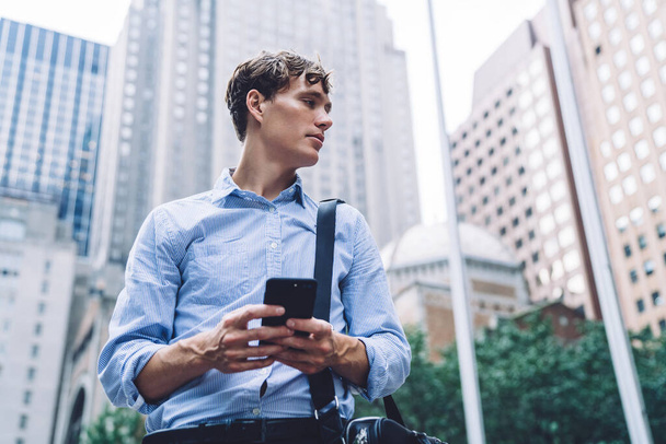 Below view of contemplative male entrepreneur in formal wear holding smartphone device and feeling pondering on received email with business information about finanicla contract, downtown area - Foto, Imagen
