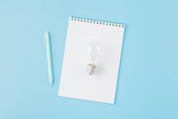 Lamp with notepad and a pen on blue background. - Foto, afbeelding