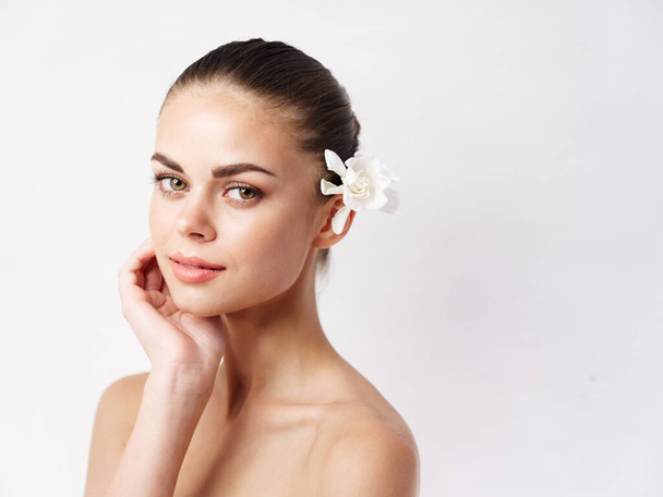 bonita mujer con hombros desnudos flor blanca en cosméticos para el cabello piel limpia - Foto, imagen