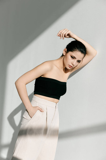 a young lady in white pants and a black top is leaning her hand on the wall - Photo, Image