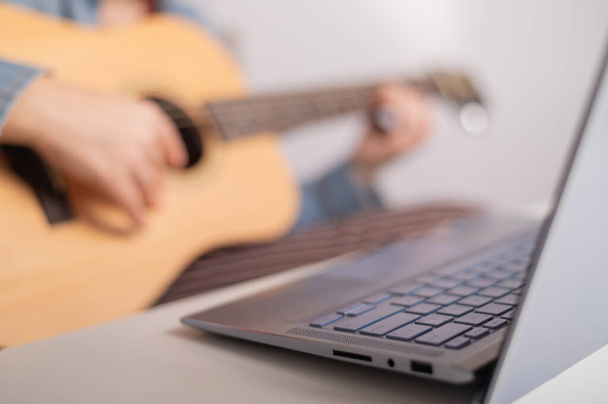 Young caucasian woman with short blonde hair playing guitar and watching training video on laptop. - 写真・画像