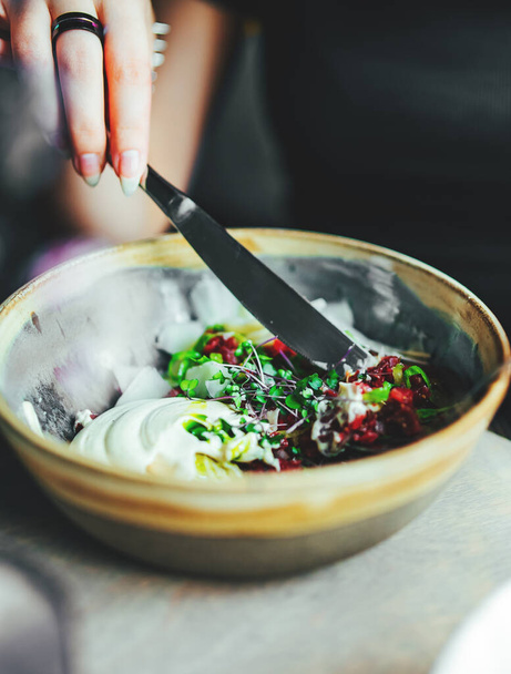 Young woman hand eating beef tartare using knife and fork fom bowl - Fotó, kép