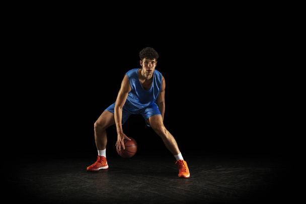 One young caucasian professional basketball player exercising with ball isolated on black background - Photo, Image