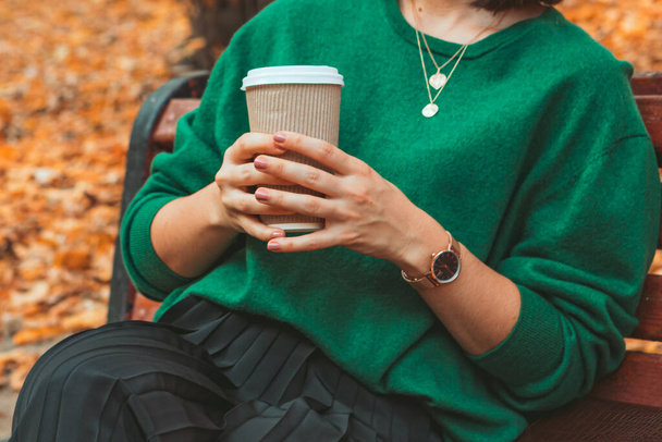 Frau sitzt an warmen Herbsttagen auf der Bank und trinkt Kaffee to go - Foto, Bild