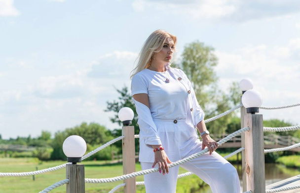 Blonde woman of plus size, American or European appearance walks at golf field, enjoying life. Young lady with excess weight, stylishly dressed at white .Natural beauty - Photo, Image
