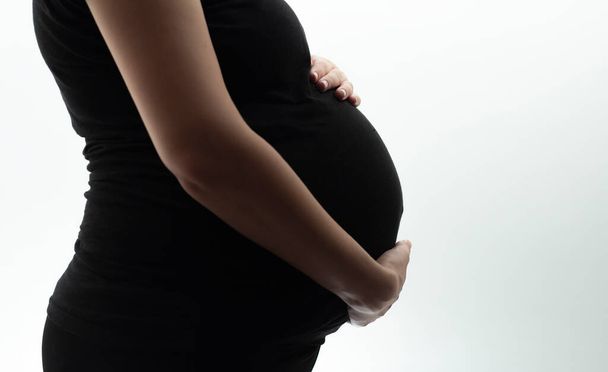 silhouette of belly of pregnant woman hugging baby with hands on white isolated background, new life concept - Foto, Imagen