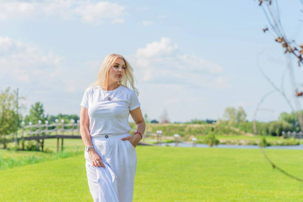 Blonde Frau mit Übergröße, amerikanischem oder europäischem Aussehen spaziert auf dem Golfplatz und genießt das Leben. Junge Dame mit Übergewicht, stilvoll in weiß gekleidet. Natürliche Schönheit - Foto, Bild