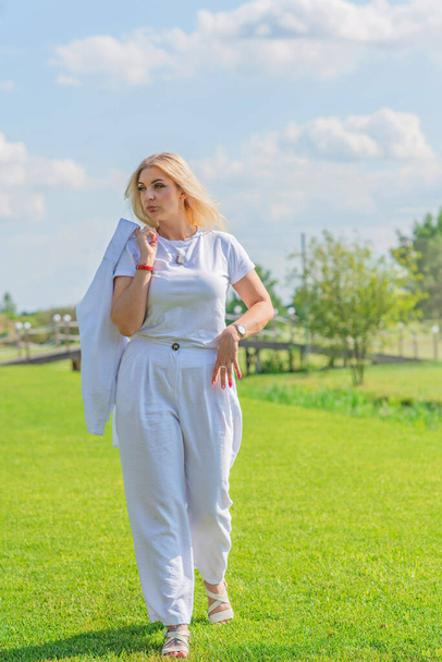 Blonde woman of plus size, American or European appearance walks at golf field, enjoying life. Young lady with excess weight, stylishly dressed at white .Natural beauty - Zdjęcie, obraz