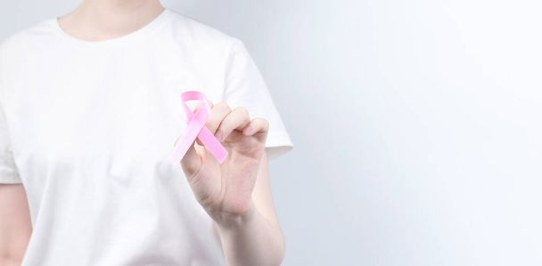 World Breast cancer day concept. Woman in white T-shirt holds pink ribbon in her hand. October Breast Cancer Awareness month. Copy space - Foto, imagen